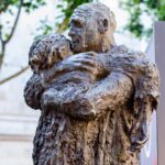 A bronze sculpture depicts a man hugging a child.